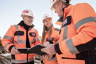 Two male and one female worker with safety clothing on a construction site discussing