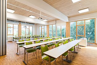 Klassenzimmer der Uni Witten. Man sieht einen möblierten Innenraum mit einer LENO-Holzdecke.