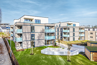 Außenansicht eines der beiden Wohngebäude mit Balkonen und einer Fassade aus Holz und Putz