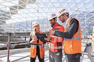 Foto zwei Männer und eine Frau auf  der Baustelle, die sich zu einem Projekt abstimmen