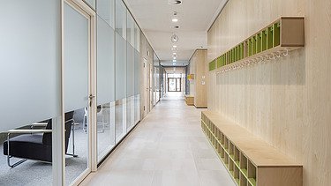 Innenaufnahme der Vinzenz-Pallotti-Schule in Friedberg. Man sieht einen Flur, eine Glas- und Holzwand und Aufbewahrungskisten an den Wänden.