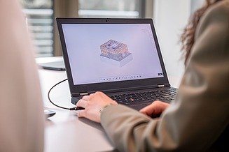 Zwei Personen sitzen vor einem Laptop auf dem ein Gebäudemodell in BIM zu sehen ist