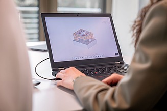 Two people are sitting in front of a laptop displaying a building model in BIM
