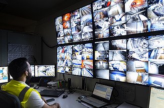 Picture of a control room with many screens and a man watching them