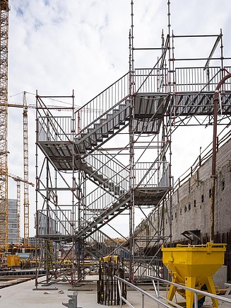 Photograph of a crane to the left and right of a concrete wall with scaffolding