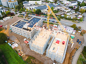 Foto der Uni Witten von außen. Man sieht die Montage großer Holzelemente aus der Vogelperspektive