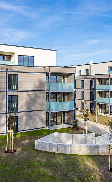 Außenansicht eines der beiden Wohngebäude mit Balkonen und einer Fassade aus Holz und Putz